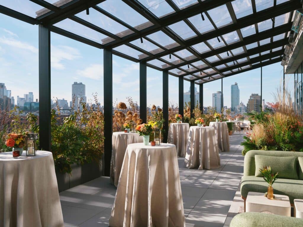 Elegant rooftop venue with tables, greenery, and Williamsburg skyline views.