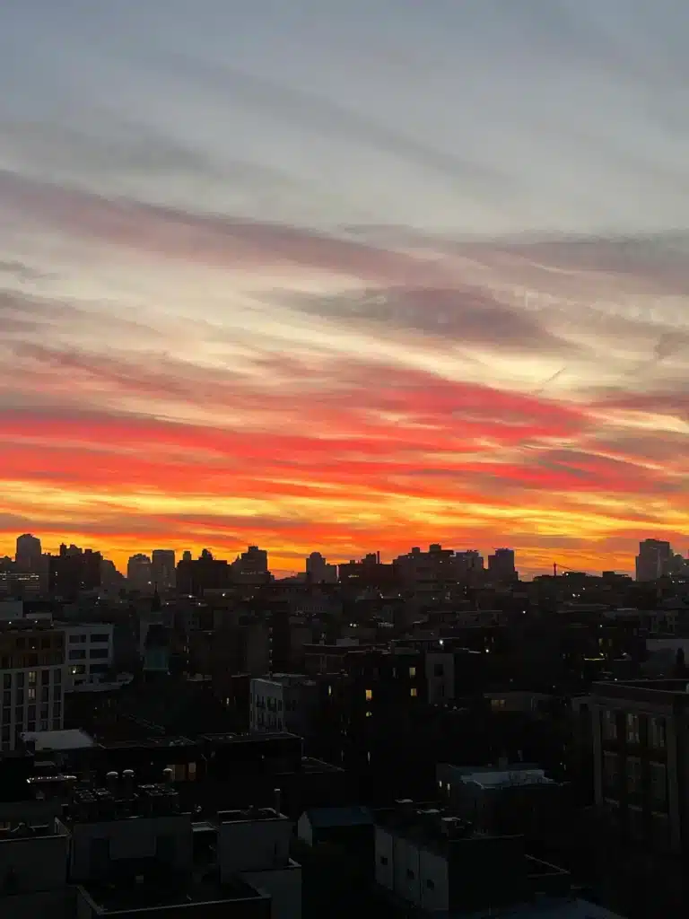 Vivid sunset over the Williamsburg skyline with red and orange streaked skies.